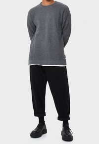 Grauer gerippter Pullover mit Rundhalsausschnitt, kombiniert mit schwarzen, weiten Hosen und schwarzen Plateau-Schuhen. Strukturierter Strickstoff.