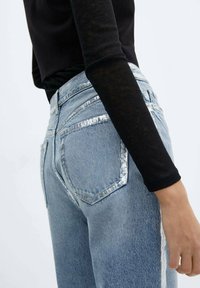 Lichtblauwe jeans met een hoge taille en zilveren accenten langs de zijnaad. Voorzien van klassieke achterzakken en een iets versleten textuur.