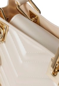 Beige gewatteerde handtas met gouden hardware. Heeft een gestructureerde vorm, contrasterende gladde binnenkant en opvallende stikdetails.