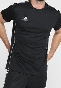 Camiseta atlética de poliéster negra de manga corta, con rayas blancas en los lados y un logo de Adidas en el pecho.