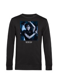 Svart långärmad tröja med kvinna i svart spetsklänning som dansar, blå bakgrund och texten "Onsdag" under bilden.