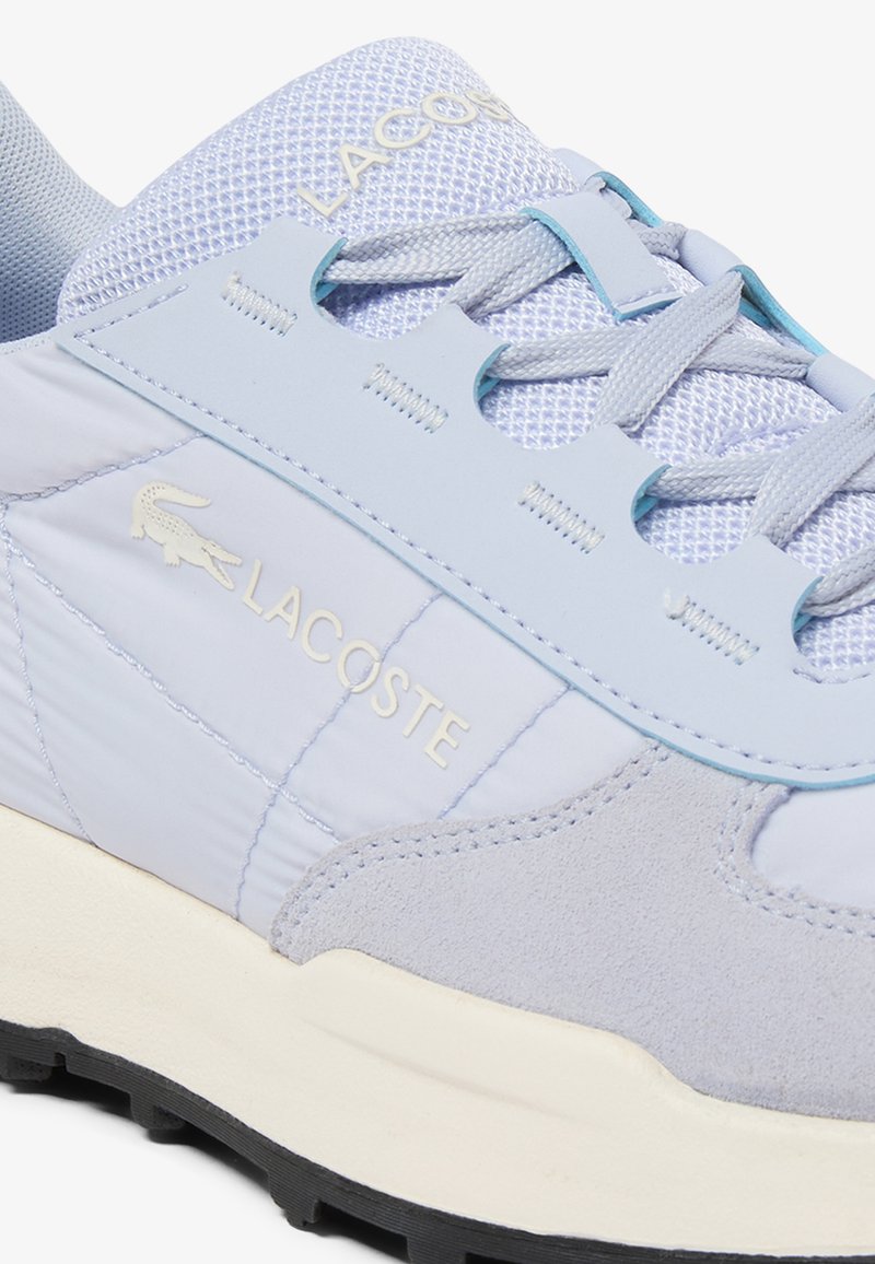 Hellblauer Lacoste-Sneaker mit Netzzunge, Wildlederspitze, cremefarbenem Zwischensohlenbereich, schwarzer Außensohle und Markenlogo an der Seite sowie Zunge.