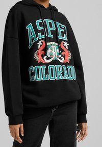 Felpa nera con cappuccio con la scritta "ASPEN COLORADO" in grande formato turchese e rosso. Il design grafico include elementi decorativi. Tessuto morbido.