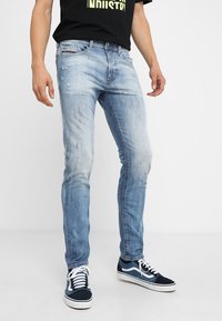 Vaalean siniset slim fit -farkut, joissa on kulutettu yksityiskohtia ja hieman haalistunut pesu. Yhdistetty tummansinisillä lenkkareilla ja mustalla T-paidalla.