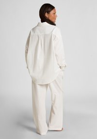 Witte relaxte outfit met een button-up blouse en wijde broek van textuurstof met subtiele verticale strepen.