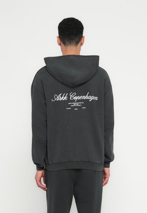 Felpa grigia scura con un grande logo bianco del marchio sul retro. Tessuto morbido, vestibilità rilassata, cappuccio regolabile e polsini a costine.
