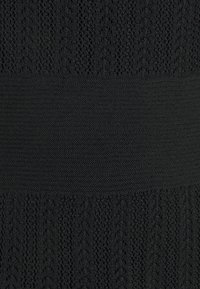 Tissu tricoté noir avec une section supérieure texturée présentant un motif en zigzag, se transitionnant vers une bande lisse en dessous.
