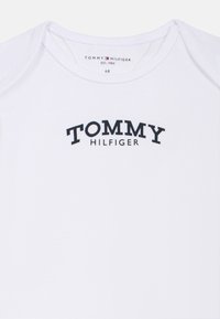 Weißes Baumwoll-T-Shirt mit einem gebogenen, schwarz gedruckten Logo "TOMMY HILFIGER" auf der Vorderseite, mit rundem Ausschnitt und kurzen Ärmeln.