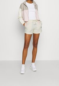 Lightweight jacket in beige, pink, and cream; fitted white t-shirt; soft cream shorts; white sneakers. Notable details include drawstrings.
