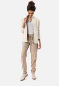 Veste zippée gris clair avec texture côtelée, associée à un jogging beige avec taille élastique et poignets, et des baskets blanches.