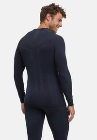 Top ajusté pour homme à manches longues en marine foncé avec des accents texturés, présentant une finition lisse, des coutures ergonomiques et des motifs réfléchissants au dos.