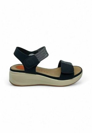 Sandalia negra con suela de plataforma y tira elástica. Plantilla blanda con perforaciones. Cierre de velcro ajustable para un ajuste seguro.