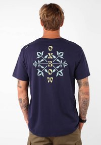 T-shirt en coton bleu marine avec un graphique floral stylisé et du texte en bleu clair et jaune au dos. Manches courtes, coupe décontractée.