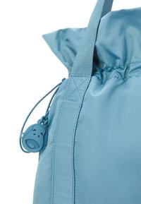 Borsa in nylon azzurro chiaro con parte superiore arricciata, dotata di chiusura con cordoncino, una tracolla robusta e un dettaglio in metallo rotondo.