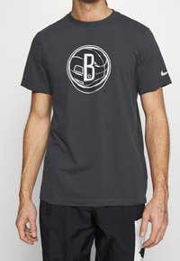 T-shirt en coton gris avec un grand logo de basket-ball blanc comportant un "B" au centre, à manches courtes et col rond.
