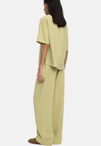 Jasno oliwkowy dwuczęściowy komplet składający się z luźnej bluzki z krótkim rękawem i szerokich spodni. Miękka, teksturowana tkanina.