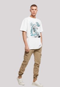 White graphic T-shirt featuring a cartoon design with a shark and characters. Paired with beige cargo pants and white sneakers.