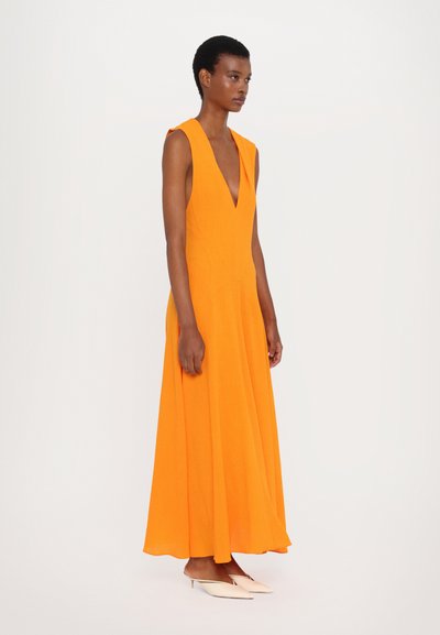Orange sleeveless maxi dress with a deep V-neck, flowing silhouette, made from lightweight fabric, paired with pointed flat shoes.