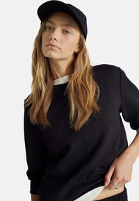 Schwarzer Sweatshirt mit Dreiviertelärmeln, ausgestattet mit einem weißen Kragen, glatter Textur und einer subtilen Naht auf der Vorderseite. Schwarze Kappe mit Logo.