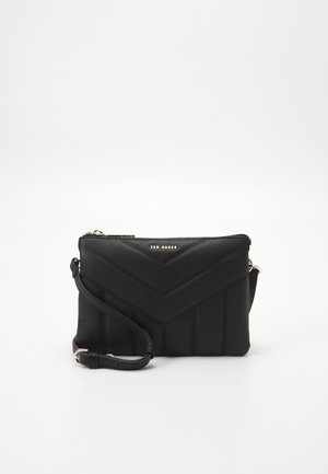 Zwarte Ted Baker crossbodytas met chevronstiksel en verstelbare riem op een effen witte achtergrond.