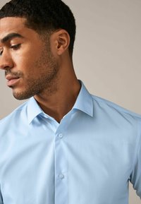 Camisa azul claro de manga corta y con botones, hecha de una tela suave. Presenta un cuello clásico y dos botones en la parte delantera. Diseño ajustado.