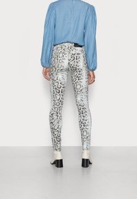 Leggings med mönster av vitt och svart ormskinn, hög midja, kombinerade med en ljusblå långärmad blus och beige stövlar med klack.