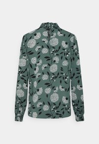 Grön blus med lång ärm och blommönster. Har vita blommor och svarta blad, samlad halsringning och elastiska manschetter.