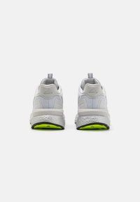 Baltas sporta apavi ar teksturētu acs augšdaļu, mīkstu papēdi un vieglu pelēku zoli, kurai ir spilgti zaļš ārmalas akcentējums.