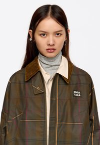 Brązowa kurtka w kratę z kołnierzem z sztruksu, z frontowym zamkiem błyskawicznym i kieszeniami bocznymi. Zawiera naszywkę z logo na klatce piersiowej.