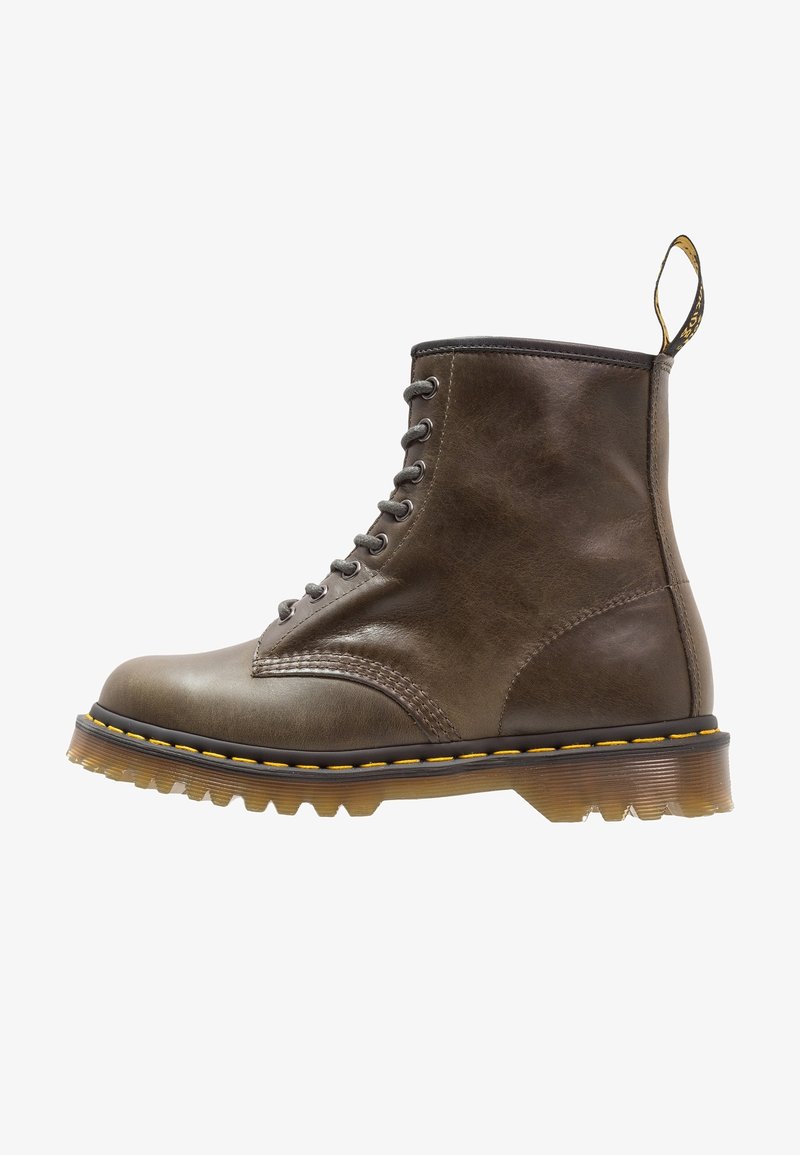 Botte montante en cuir marron avec coutures jaunes, semelle translucide à rainures, et languette arrière noire et jaune.