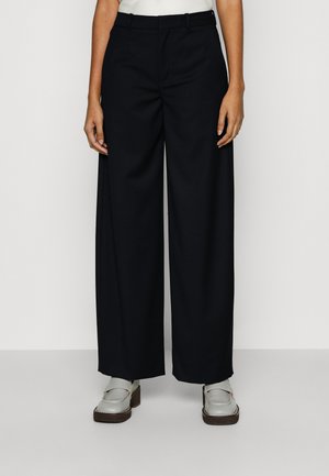 Black wide-leg trousers made of soft fabric, featuring a fitted waist and structured design. Paired with light gray flat shoes.