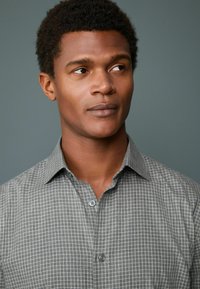 Gray checkered shirt with a button-down collar and two buttons visible. The fabric appears smooth with a subtle texture. Background is gray.