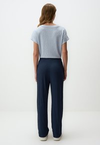 Lichtblauw gestructureerd T-shirt met korte mouwen, gecombineerd met donkerblauwe geplooide brede broek en witte sneakers, bekeken vanuit de achterkant.
