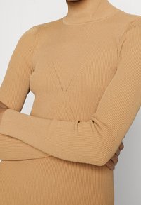 Abito maglione beige a coste con una vestibilità aderente, maniche lunghe e un collo alto. Presenta un motivo testurizzato con linee verticali e un design incrociato.