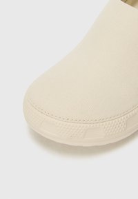 Botte beige à enfiler avec une tige en toile texturée et un bout rond. La semelle en caoutchouc est dotée de petits points de grip pour une meilleure traction.