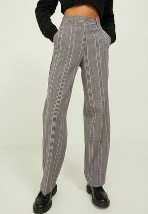 Persoon die een hoge taille geblokte broek met rechte pijpen draagt, met handen in de zakken en zwarte leren schoenen, gecombineerd met een zwart cropped trui.