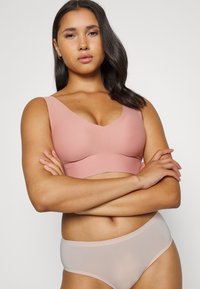 Ljusrosa stretchbh med V-ringning, breda band och sömlösa kanter, tillsammans med ett ljusrosa genomskinligt trosset med mjuk textur.