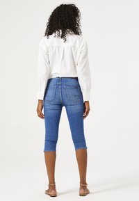 Lichtgewicht witte button-up shirt met lange mouwen, gecombineerd met strakke, knielange blauwe denim leggings met achterzakken en opgerolde manchetten.