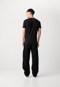 Black short-sleeve t-shirt with a smooth texture, paired with loose black pants and white sneakers, showcasing a minimalist design.