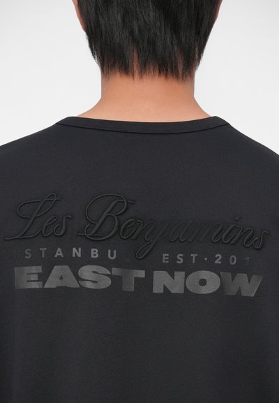 Melna kokvilnas T-krekls ar reljefiem uzrakstiem uz aizmugures: "Les Benjamins ISTANBU EST. 201" un "EAST NOW" kontrastējošā pelēkā krāsā.
