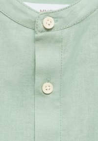 Camicia button-up verde chiaro con colletto, dotata di due bottoni bianchi e un tessuto strutturato e intrecciato.