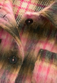 Gros plan d'un tissu à carreaux flou multicolore rose, marron et beige avec des boutons noirs et une poche cousue.
