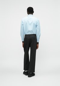 Cămașă cu dungi de culoare albastru deschis, cu mâneci lungi, asortată cu pantaloni negri. Pantalonii au buzunare și sunt largi; pantofii negri completează ținuta.