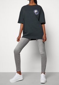 Camiseta de algodón negra de gran tamaño con gráfico de sol yin-yang en el pecho, combinada con pantalones ajustados grises y zapatillas de plataforma blancas.
