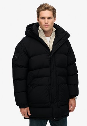 Chaqueta de plumas negra con capucha, con un diseño acolchado, cierre de cremallera y dos bolsillos frontales. Fabricada con un material suave e insulated.