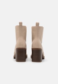 Bottines en cuir beige avec un bout arrondi, des coutures latérales et un talon bloc texturé. Dotées d'une languette à l'arrière.