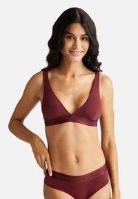 Bralette wireless bordeaux con spalline larghe e scollatura a V profonda. Presenta una consistenza morbida e un bordo con logo impresso per comfort e supporto.