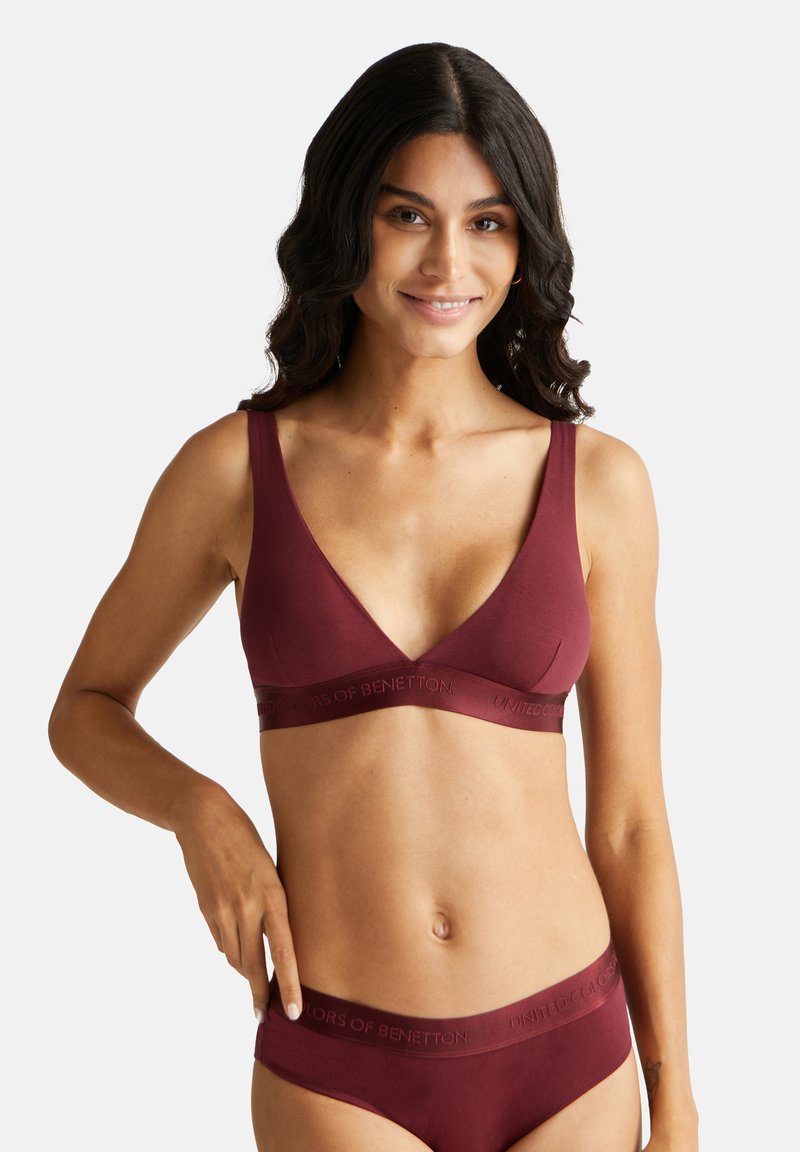 Bralette wireless bordeaux con spalline larghe e scollatura a V profonda. Presenta una consistenza morbida e un bordo con logo impresso per comfort e supporto.
