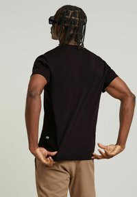 Camiseta negra de manga corta hecha de algodón, con cuello redondo, corte ajustado y una pequeña etiqueta de marca cerca del dobladillo en el lado.
