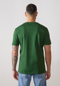 Grønn bomull T-skjorte med korte ermer, rund hals og enkelt design. Kombinert med lyseblå denimjeans, som viser en avslappet passform.